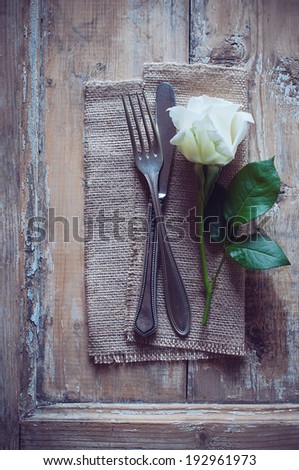Vintage cutlery, antique silverware, fork, knife and a rose flower with rough cloth on an old wooden background