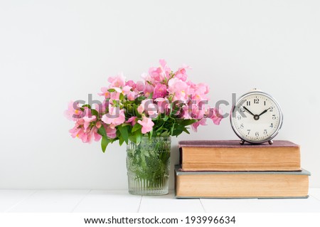 Retro home decor: a stack of books, flowers and a vintage alarm clock on a white wall shelf