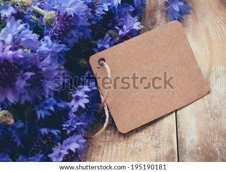 Rustic bouquet of blue cornflowers and brown cardboard tag on vintage wooden board