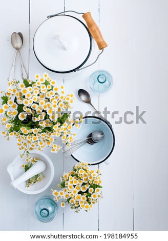 Chamomile flowers, white enamel cookware, glass bottles, vintage spoons on a white wooden background, cozy home rustic decor, vintage country living