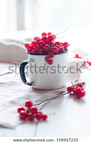 Fresh natural organic red currants in a white enamel mug and white linen cloth on a wooden table, seasonal berries, rustic food.