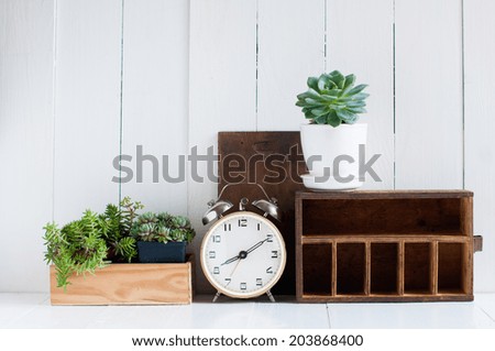 Vintage home decor: old wooden boxes, houseplants, alarm clock on white wooden board, retro home interior.