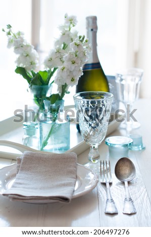 Vintage festive table setting, white matthiola flowers, wineglasses, cutlery and a bottle of champagne on the table