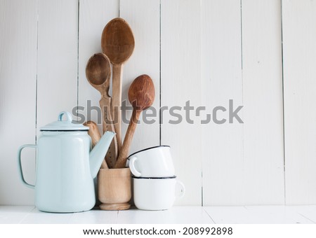 Home kitchen still life: Vintage coffee pot, enamel mugs and antique rustic wooden spoons on a barn wall background, soft pastel colors.