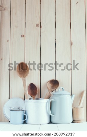 Home kitchen still life: Vintage coffee pot, enamel mugs and antique rustic wooden spoons on a barn wall background, soft pastel colors.