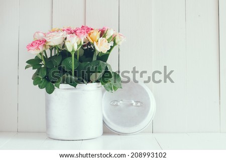 Vintage home arrangement, bright summer roses in aluminium jar on a barn wall background