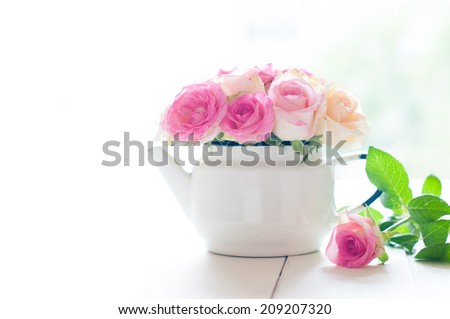 Bouquet of yellow and pink roses in a white enameled vintage teapot in bright sunlight on a white wooden table, rustic home decoration background