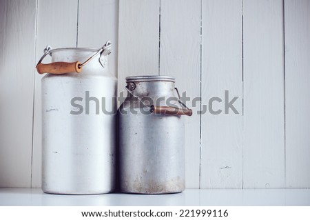 Two old vintage aluminum milk cans, painted white wooden board, rustic background