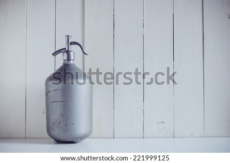 An old vintage aluminum siphon, antique seltzer soda bottle, painted white wooden board, rustic background