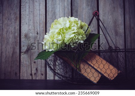 White hydrangea flowers and vintage books in a metal basket on a wooden background.