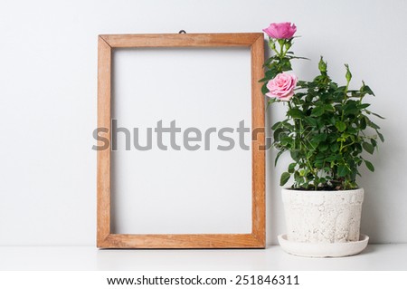 Vintage blank wooden frame and rose in a pot on a white wall