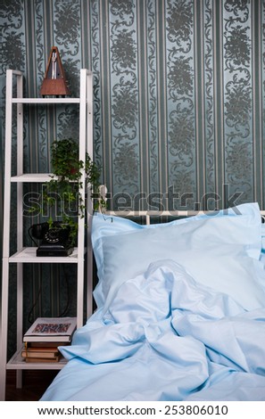 Cozy bedroom interior, double bed with light blue bed linen, pillows and shelves with vintage decor