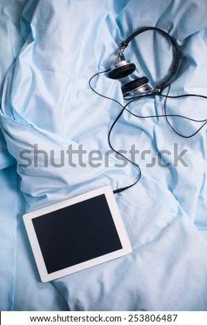 Tablet with headphones on a light blue linen, reading and music in bed