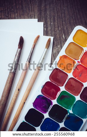 Watercolor paints and brushes, painting tools on an old wooden board.