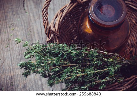 Brown glass pharmacy bottle and thyme herb in a wicker basket vintage style on old wooden board.