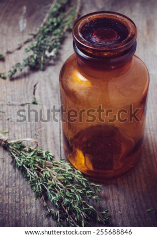 Brown glass pharmacy bottle and thyme herb in vintage style on old wooden board.