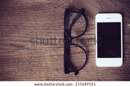 Smartphone and reading glasses on an old wooden board, hipster style