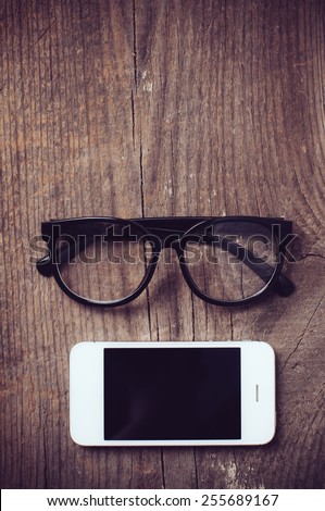 Smartphone and reading glasses on an old wooden board, hipster style