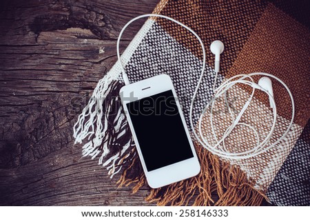 White smart phone with headphones and brown plaid on an old wooden board