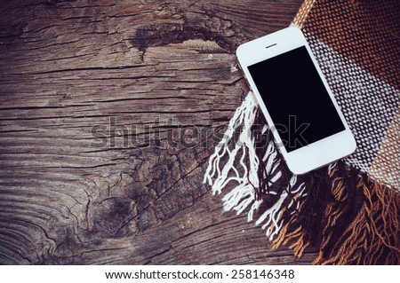 White smartphone, and brown plaid on an old wooden board