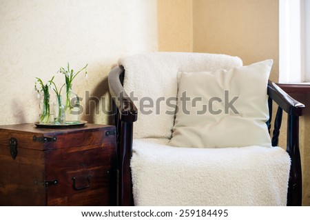 Spring flowers snowdrops in glass bottles, home interior, vintage chair with a pillow
