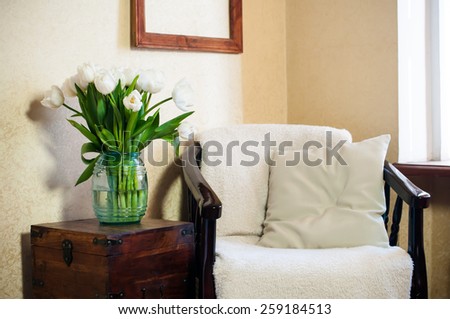 Home interior, vintage chair with a pillow and a bouquet of white tulips