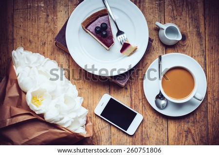 Bouquet of tulips, coffee with milk, cheesecake and smartphone on a shabby wooden floor, hipster lifestyle