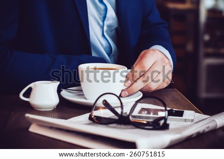 Businessman in a blue jacket with a cup of coffee, reading glasses, newspaper and smartphone in a cafe at the table, close-up
