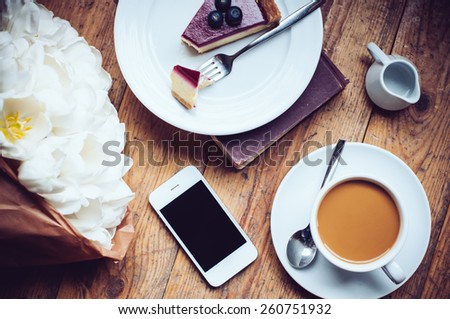 Bouquet of tulips, coffee with milk, cheesecake and smartphone on a shabby wooden floor, hipster lifestyle