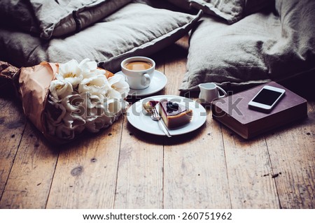 Pillows, a bouquet of tulips, coffee with milk, cheesecake and smartphone on a shabby wooden floor. Hipster lifestyle