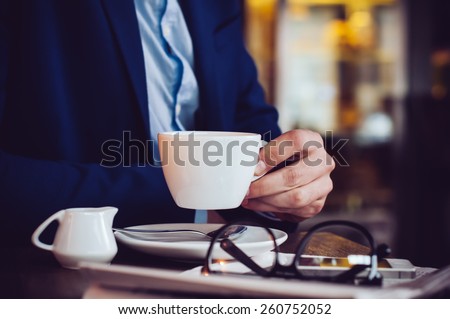 Businessman in a blue jacket with a cup of coffee, reading glasses, newspaper and smartphone in a cafe at the table, close-up