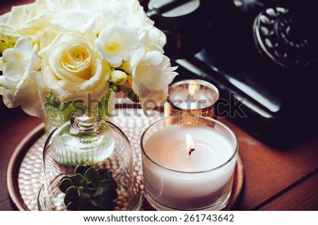 Bouquet of white flowers in a vase, candles on a copper vintage tray, old rotary phone, retro home decor