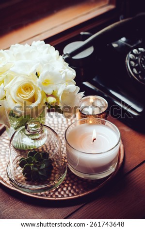 Bouquet of white flowers in a vase, candles on a copper vintage tray, old rotary phone, retro home decor