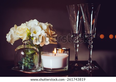 Bouquet of flowers in a vase, candles and champagne glasses on a tray, vintage home decor on an a table, dark tones