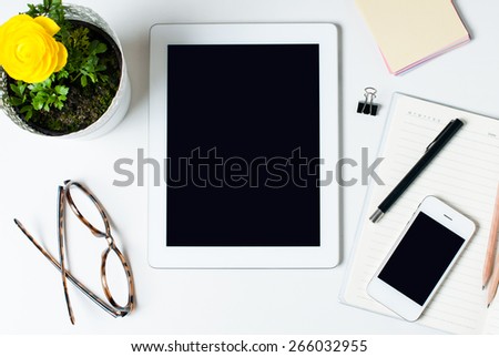 Desktop, home office: a tablet, notebooks, glasses, smart, flower, pens and pencils on a white background
