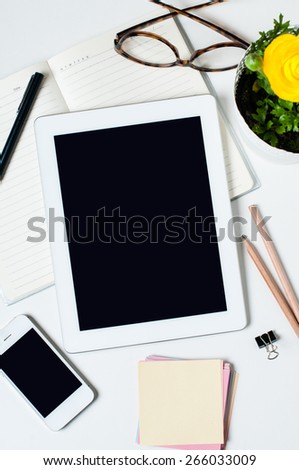 Desktop, home office: a tablet, notebooks, glasses, smart, flower, pens and pencils on a white background