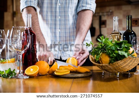 Man cuts oranges for making sangria for home party, home kitchen interior. Homemade food and drinks