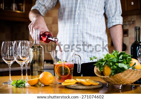 Man pouring red wine into a carafe, making sangria for home party, home kitchen interior. Homemade food and drinks