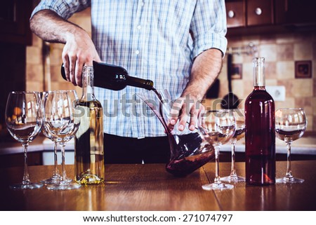 Man pouring red wine from bottle into a decanter, home kitchen interior, bottles of wine