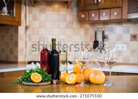 Three bottles of wine: white, rose and red, empty glasses and fruits on the kitchen table in a home kitchen interior