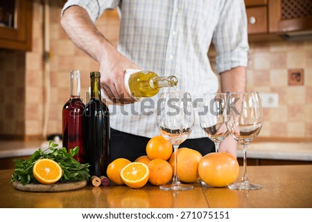 Man pours white wine from a bottle into a glass, home kitchen interior, wine party.