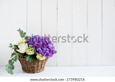 Big bouquet of fresh flowers, purple hydrangeas and white roses in a wicker basket on an white wooden board, vintage style