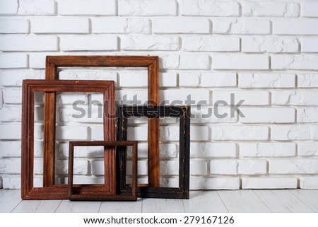 Several old empty wooden frames on a  white brick wall background, room interior.