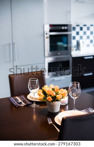 Simple home table setting with flowers, glasses and cutlery in a kitchen interior.