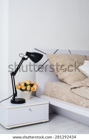 Bright white bedroom interior, cozy bed with beige linen, flowers on a bedside table, closeup