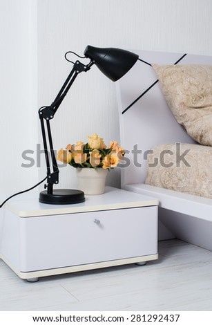 Bright white bedroom interior, cozy bed with beige linen, flowers on a bedside table, closeup
