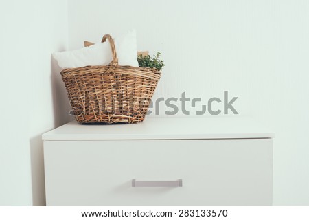 Wicker basket with a pillow and green home plant at the white wall on the chest of drawers, modern home interior decor with copy space
