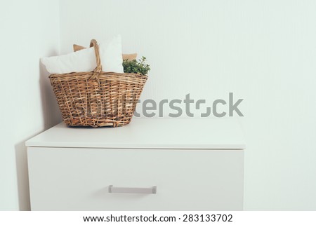 Wicker basket with a pillow and green home plant at the white wall on the chest of drawers, modern home interior decor with copy space