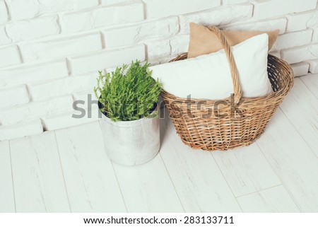 Wicker basket with a pillow and green home plant at the white brick wall on the floor, rustic home interior decor with copy space