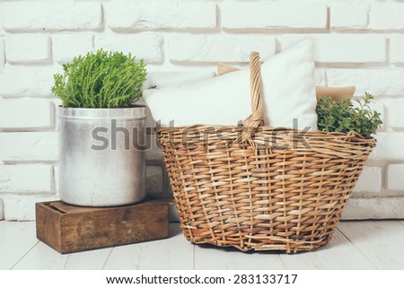 Wicker basket with a pillow and green home plant at the white brick wall on the floor, rustic home interior decor
